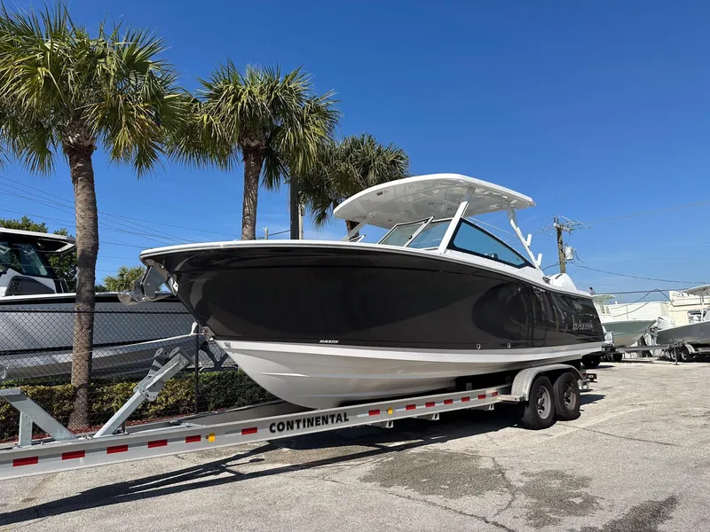 Slide: The Image of 2024 Blackfin 272DC boat on trailer, parked under palm trees, clear blue sky. - 2