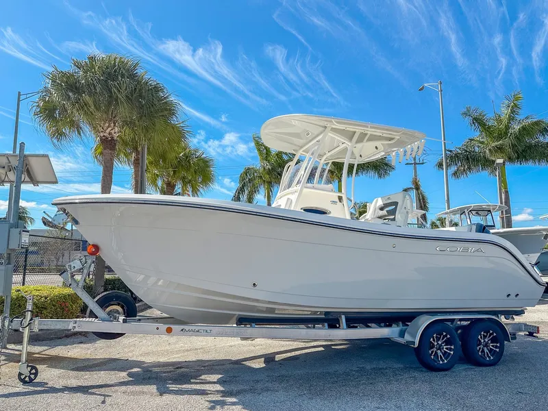 Slide: The Image of 2024 Cobia 220 CC boat on trailer, parked under palm trees, clear blue sky. - 1