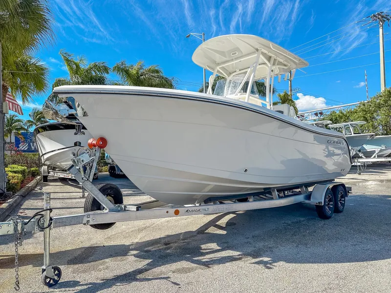 Slide: The Image of 2024 Cobia 220 CC boat on trailer, sunny day, palm trees in background. - 2