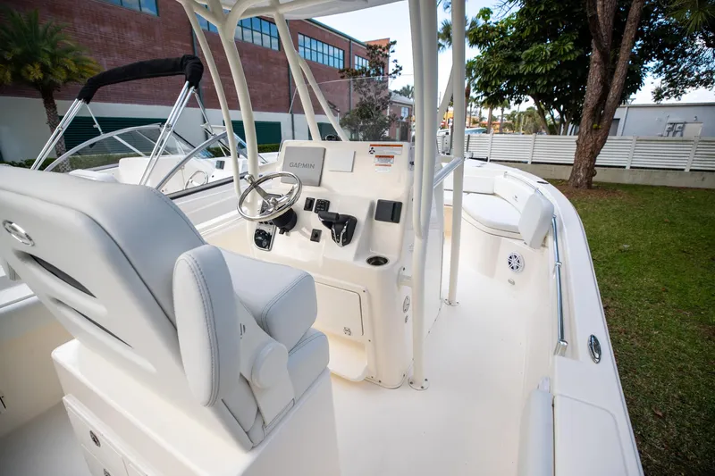 Slide: The Image of 2024 Cobia 220 CC boat interior with steering console and seating, parked on grass. - 18