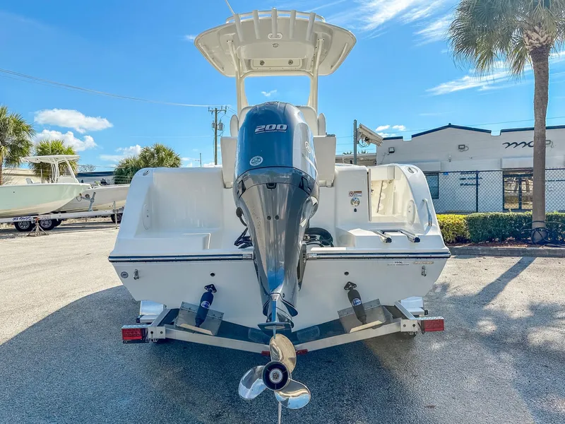 Slide: The Image of 2024 Cobia 220 CC boat with powerful outboard motor, parked outdoors under clear blue sky. - 5