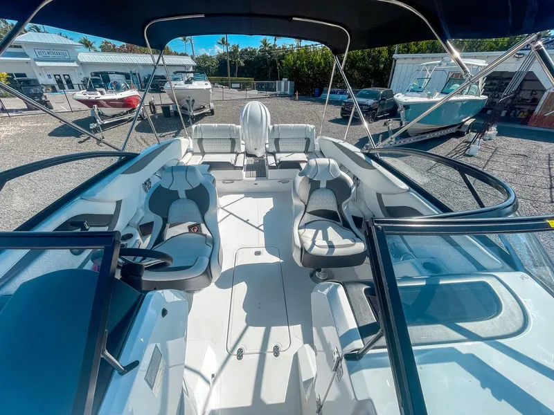 Slide: The Image of 2024 Hurricane SunDeck 2600 OB boat interior with seating and steering wheel, docked outdoors. - 17