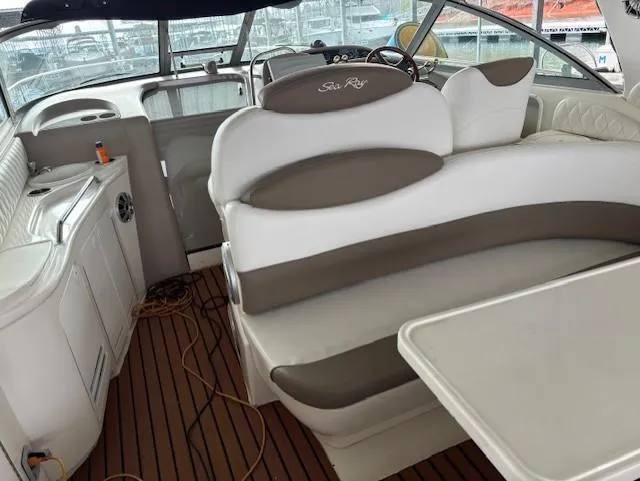 Slide: The Image of 2000 Sea Ray 340 Sundancer interior with white and beige seating, wooden flooring, and helm. - 11