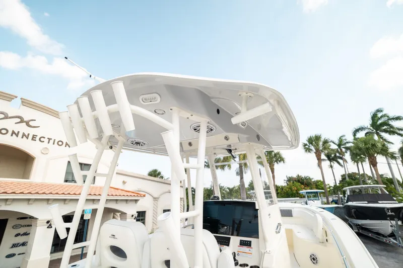 Slide: The Image of 2024 Cobia 301 CC boat with T-top, parked near a dealership, palm trees in background. - 14
