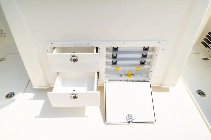 Slide: The Image of 2024 Cobia 301 CC boat storage compartments with open drawers and tackle boxes. - 32