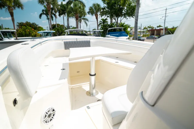 Slide: The Image of 2024 Cobia 301 CC boat interior with seating and table, surrounded by palm trees. - 42