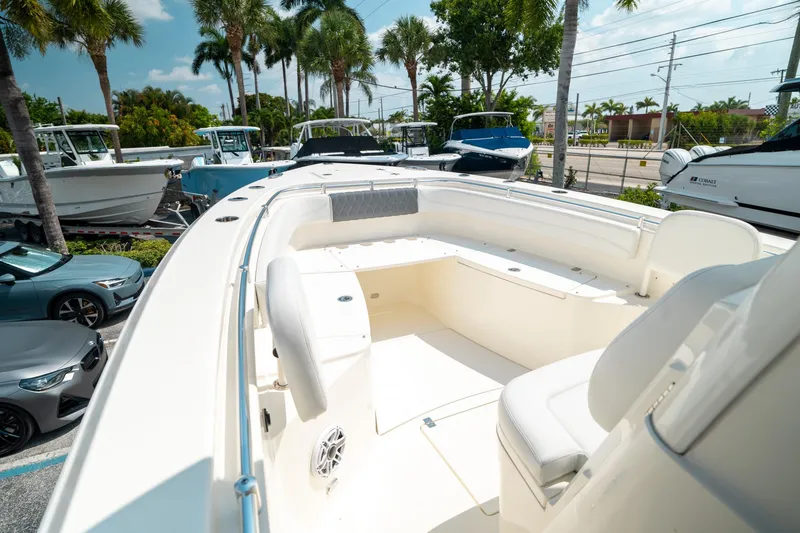 Slide: The Image of 2024 Cobia 301 CC boat interior with seating, surrounded by palm trees and parked vehicles. - 39