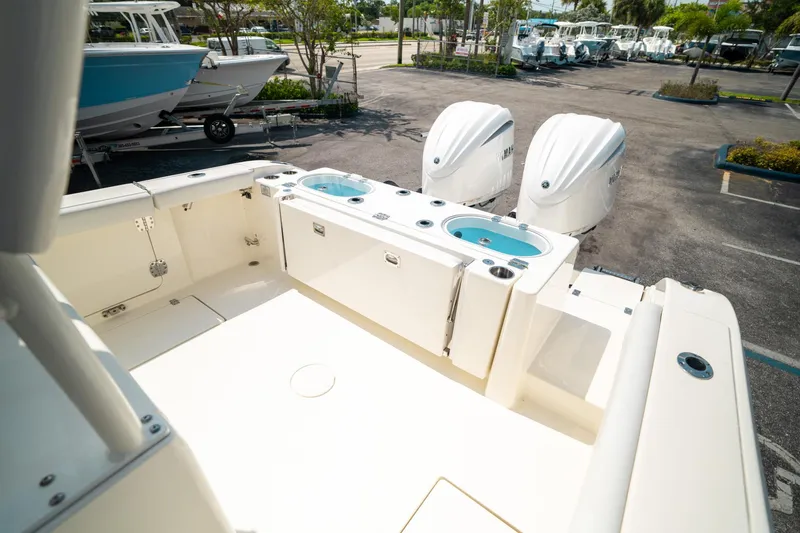 Slide: The Image of 2024 Cobia 301 CC boat with dual engines, spacious deck, and livewell in a marina setting. - 23