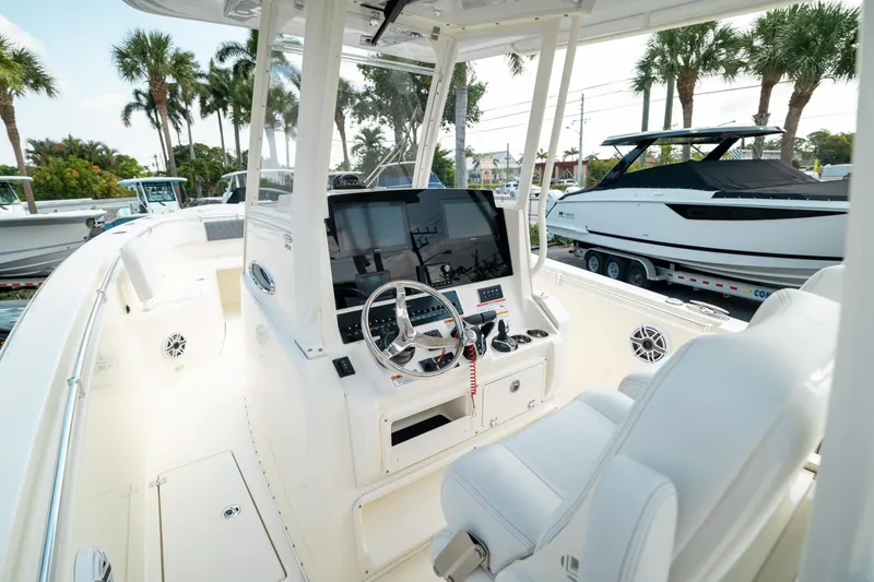 Slide: The Image of 2024 Cobia 301 CC boat interior with steering console, white seating, and palm trees in background. - 11