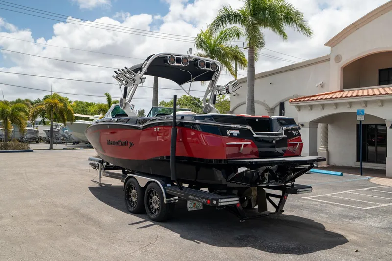 Slide: The Image of 2019 MasterCraft X-Star boat on trailer, parked outdoors near palm trees and building. - 5
