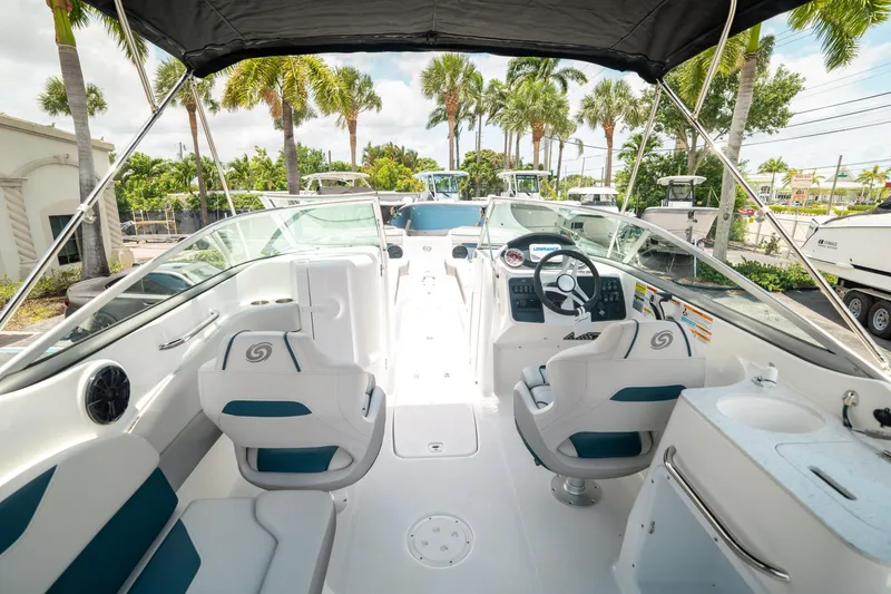 Slide: The Image of 2024 Hurricane SunDeck 2400 OB boat interior with seating and steering wheel, surrounded by palm trees. - 9