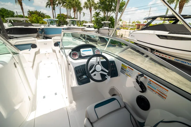 Slide: The Image of 2024 Hurricane SunDeck 2400 OB boat interior with steering wheel and dashboard, docked among other boats. - 24