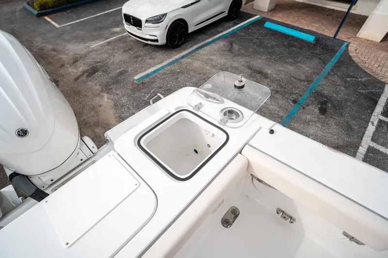 Slide: The Image of 2025 Sea Hunt Gamefish 27 FS boat with open storage compartment, parked near a white car. - 14