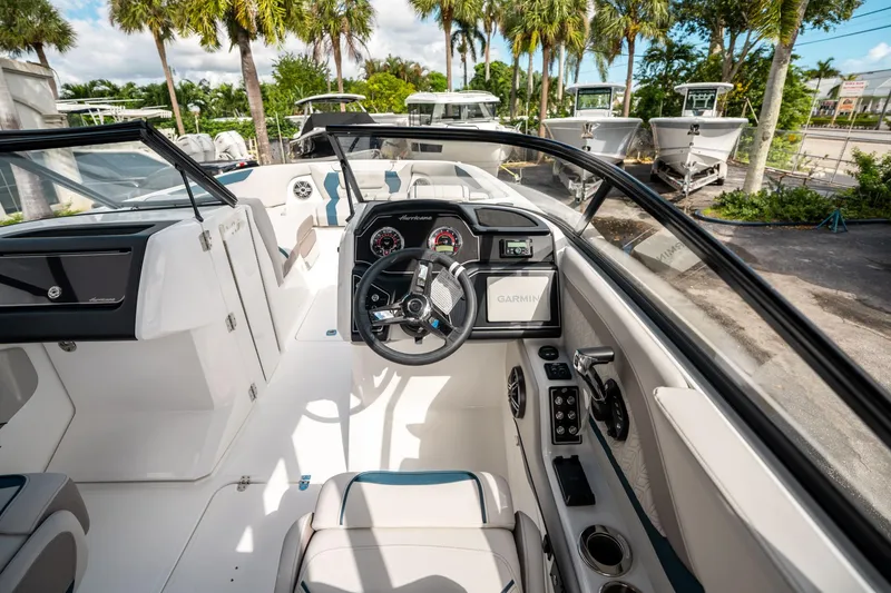 Slide: The Image of 2025 Hurricane SunDeck 2600 OB boat interior with steering wheel and dashboard, surrounded by palm trees. - 18