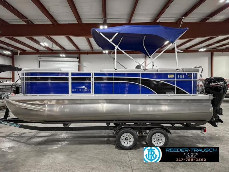 Slide: The Image of 2023 Bennington 208 SL pontoon boat with blue canopy on trailer in showroom. - 11