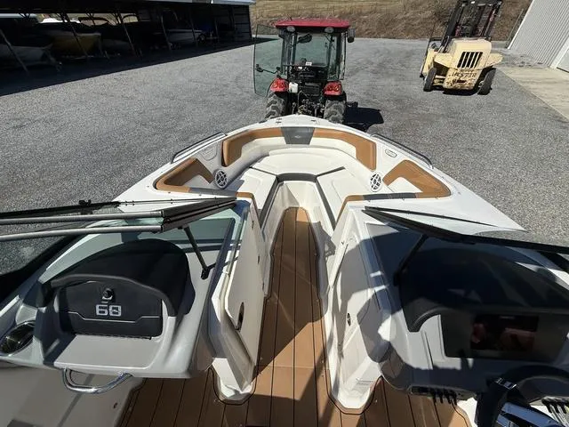 Slide: The Image of 2025 Chaparral 23 SSi boat interior with tan accents, parked near tractors. - 16