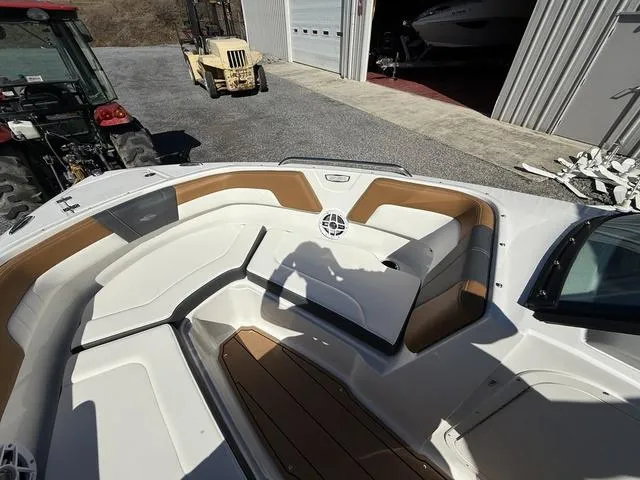 Slide: The Image of 2025 Chaparral 23 SSi boat interior with tan and white seating, parked near a garage. - 18