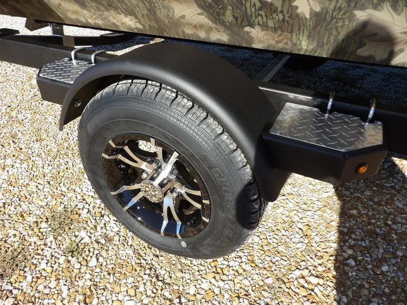 Slide: The Image of 2025 Crestliner XFC 189 trailer wheel with black alloy rim on gravel surface. - 35