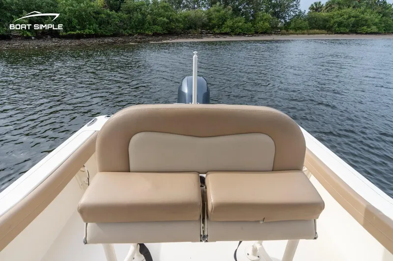 Slide: The Image of 2023 Scout 215 XSF boat with tan seating, on calm water near a wooded shoreline. - 11