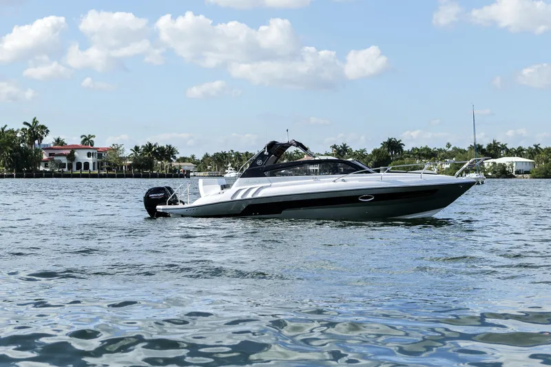 Slide: The Image of 2025 Hanover 305 Outboard Alpine Gray Ultimate Sport Edition boat on a serene waterway. - 10