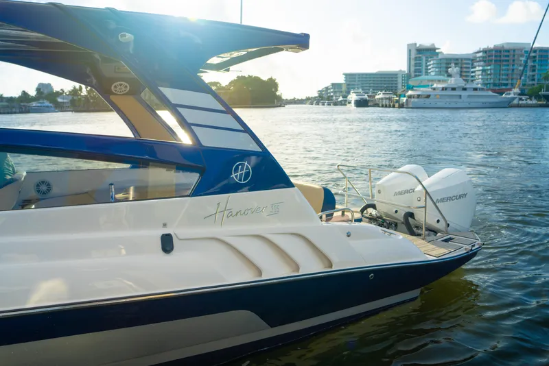 Slide: The Image of 2025 Hanover 305 Outboard Alpine Gray Ultimate Sport Edition boat on water, cityscape background. - 18