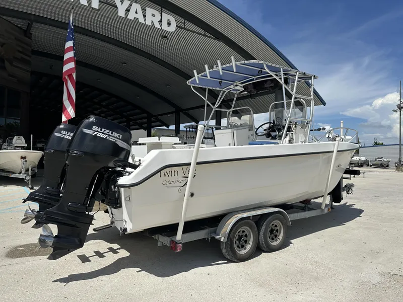 Slide: The Image of 2005 Twin Vee 22 boat with Suzuki engines on a trailer, parked outside a boatyard. - 1