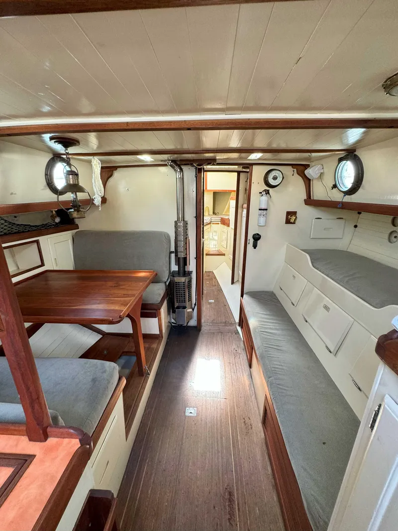 Slide: The Image of 1975 Westsail 32 interior with wooden furnishings, cozy seating, and nautical decor. - 17