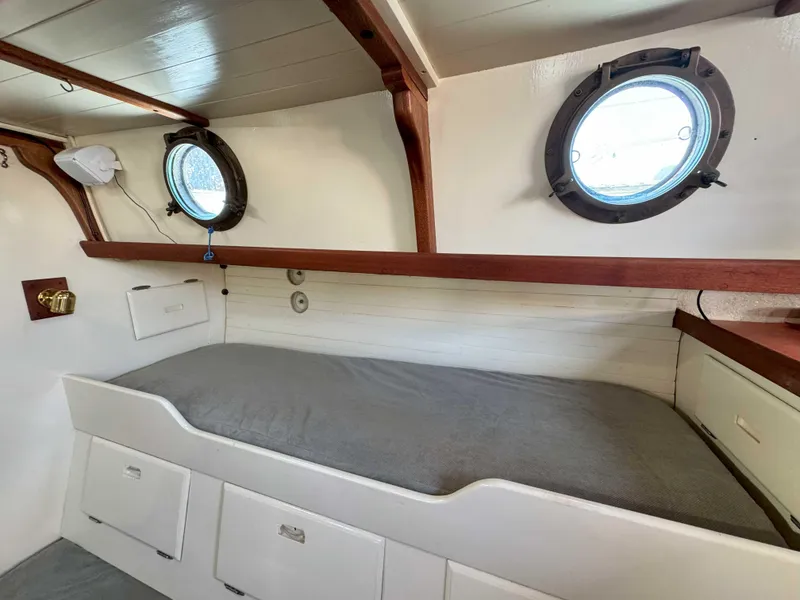Slide: The Image of 1975 Westsail 32 interior cabin with portholes, wooden accents, and a cozy berth. - 21