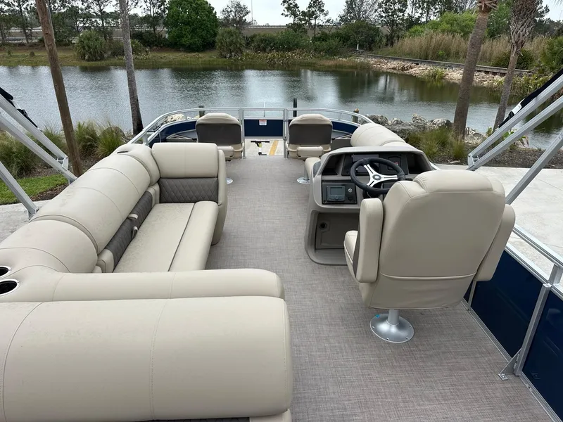 Slide: The Image of 2025 Sun Tracker Fishin' Barge 20 DLX pontoon boat with beige seating, near a serene lake. - 4