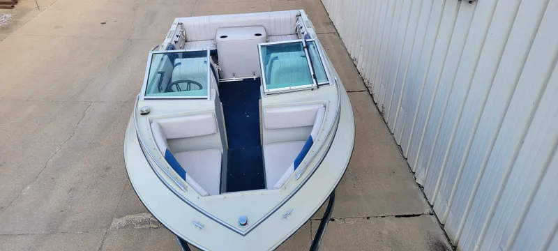 Slide: The Image of 1986 Four Winns 160 Freedom boat with open bow seating, docked beside a building. - 2