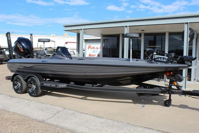 Slide: The Image of 2025 Skeeter ZXR21 boat on trailer, parked outside a building under a clear sky. - 1