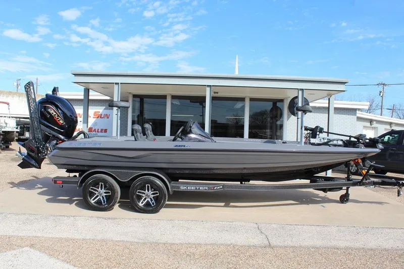 Slide: The Image of 2025 Skeeter ZXR21 boat on trailer, parked outside a building under a clear blue sky. - 2
