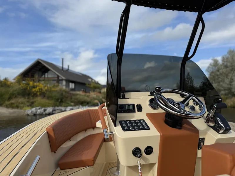 Slide: The Image of AlCustom Levanzo 25 boat interior, 2025 model, with steering wheel and controls, near a lakeside cabin. - 12