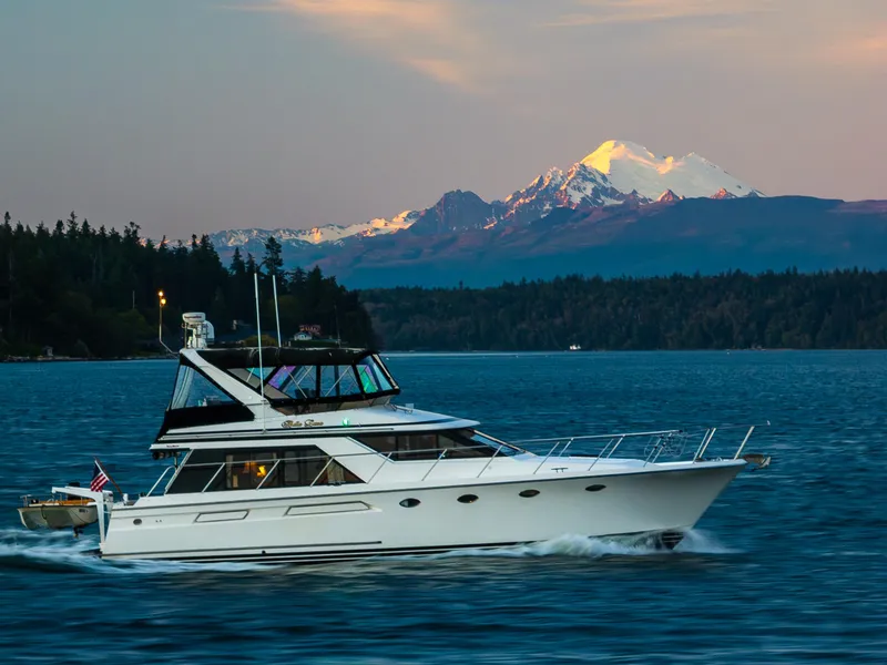 The Image of 1990 Ocean Alexander 48 Cockpit Motoryacht cruising on scenic water with mountain backdrop. - 0