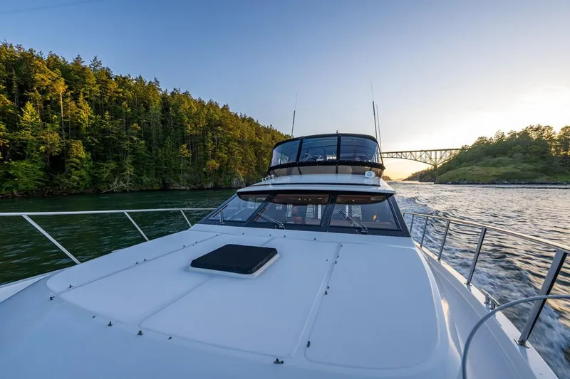 Slide: The Image of 1990 Ocean Alexander 48 Cockpit Motoryacht cruising near a scenic forested shoreline and bridge. - 20