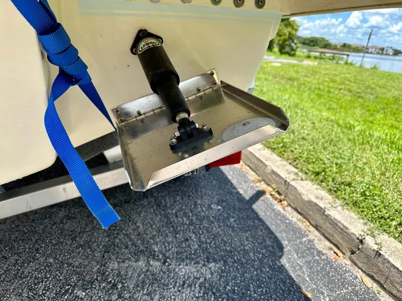 Slide: The Image of Trim tab of 2023 Scout 215 Dorado boat on a trailer, near a grassy area. - 21