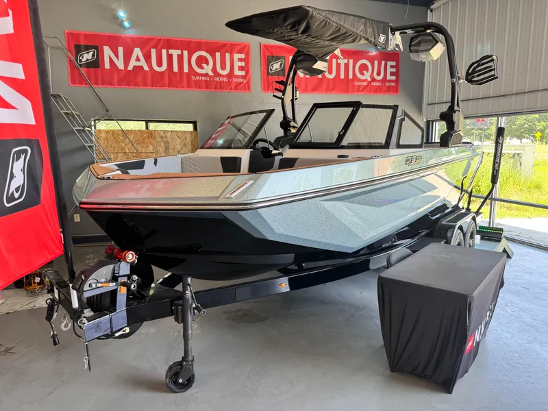Slide: The Image of 2025 Nautique Super Air Nautique GS20 boat displayed in showroom with red Nautique banners. - 2