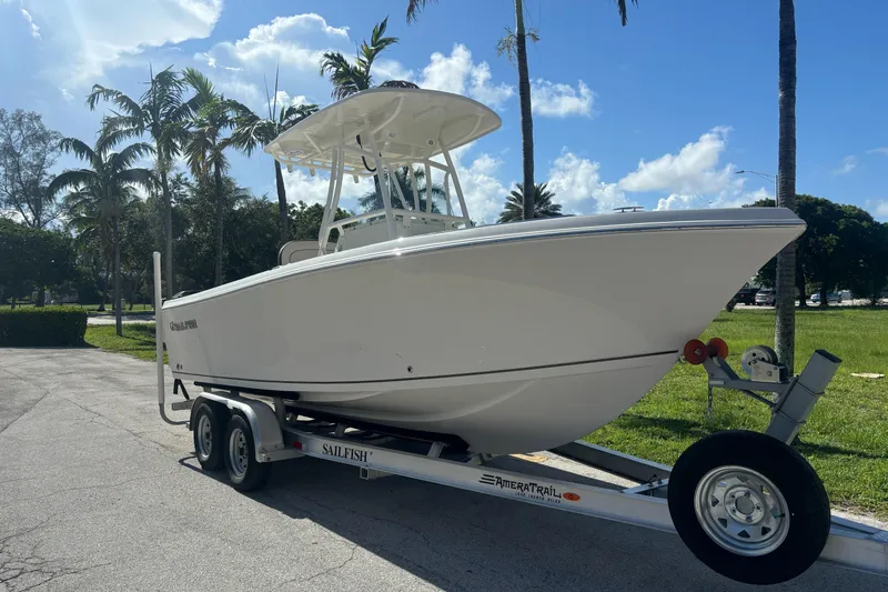 Slide: The Image of 2023 Sailfish 220 CC boat on trailer, parked near palm trees under a blue sky. - 0