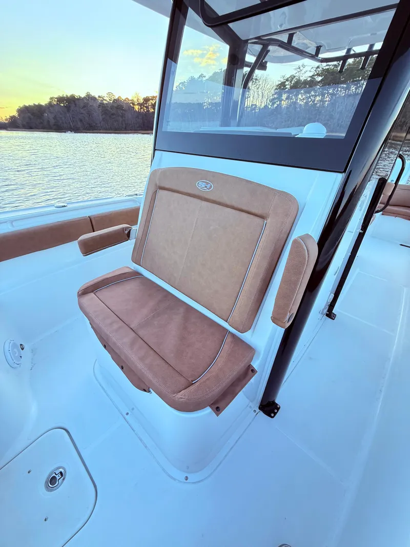Slide: The Image of 2023 Sea Hunt Ultra 305 SE boat interior with tan seating, near water at sunset. - 16