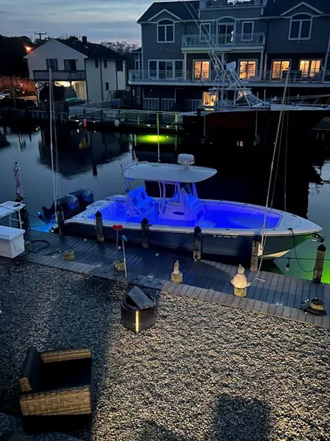 Slide: The Image of 2018 Cobia 277 Center Console boat docked, illuminated with blue lights, near waterfront homes. - 4