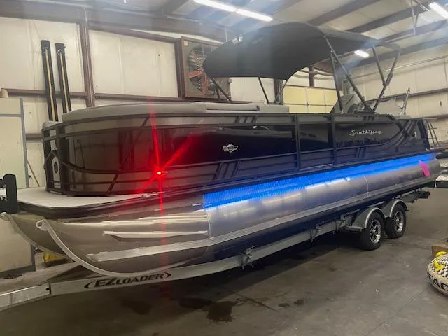 Slide: The Image of 2025 South Bay 500 pontoon boat on trailer in warehouse, featuring blue LED lights. - 3