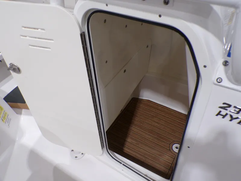 Slide: The Image of 2024 NauticStar 231 Hybrid boat storage compartment with open door and wood flooring. - 20