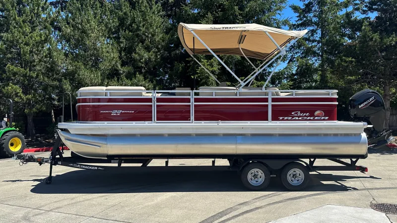 The Image of 2025 Sun Tracker Party Barge 22 DLX pontoon boat on trailer, parked outdoors. - 0