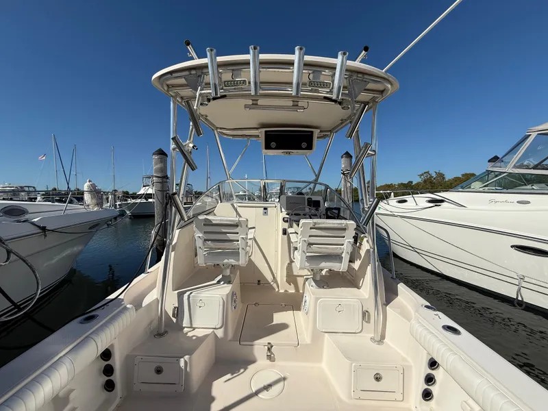 Slide: The Image of 2006 Cobia 250 Walk-Around boat docked, featuring spacious deck and seating under clear blue sky. - 12