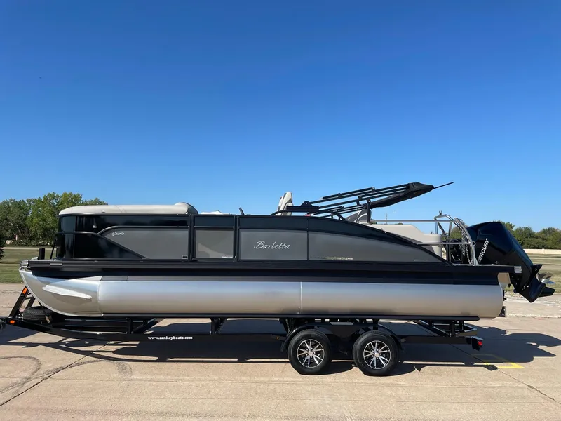 Slide: The Image of 2024 Barletta Cabrio 22UC pontoon boat on trailer, parked outdoors under clear blue sky. - 2