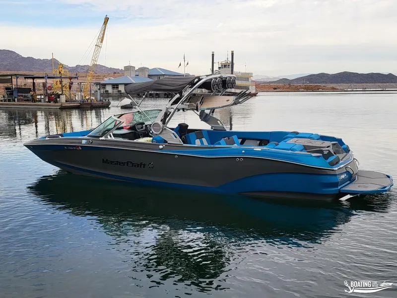 Slide: The Image of 2021 MasterCraft X26 boat docked on calm water, featuring sleek design and blue accents. - 13