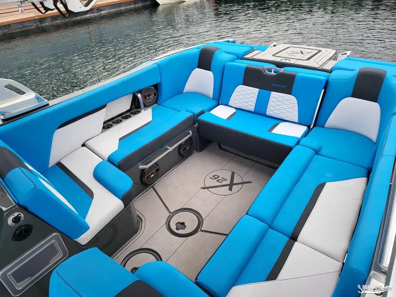 Slide: The Image of 2021 MasterCraft X26 boat interior with blue and white seating, docked by the water. - 15