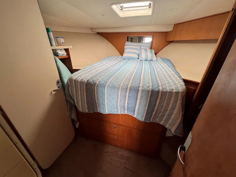 Slide: The Image of 1999 Luhrs 360 Convertible cabin with striped bedding and wooden storage. - 16