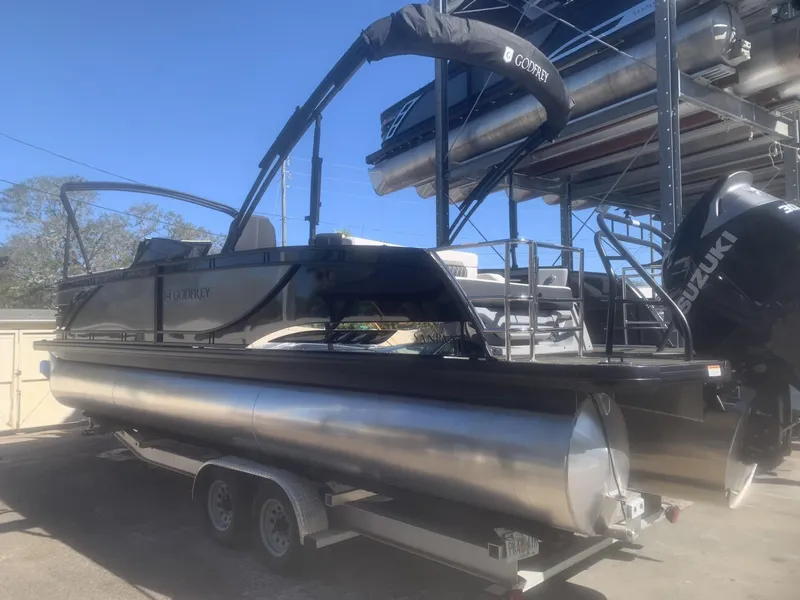Slide: The Image of 2025 Godfrey San Pan 2700 DFLW pontoon boat on trailer, featuring Suzuki outboard motor. - 0