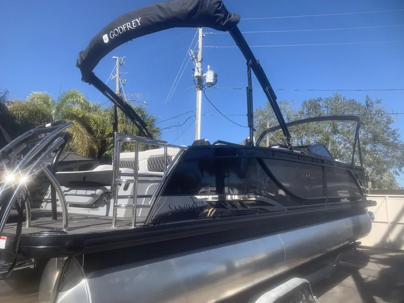 Slide: The Image of 2025 Godfrey San Pan 2700 DFLW pontoon boat with canopy, parked outdoors. - 1